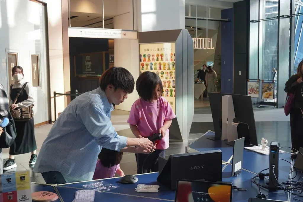 展示ブースでゲームパッドを持つ子どもに操作を説明する様子